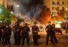 Police officers in riot gear near burning car