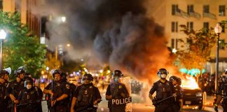 Police officers in riot gear near burning car