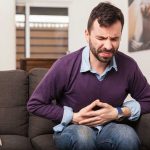 Man sitting on couch, holding stomach in pain