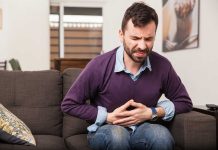 Man sitting on couch, holding stomach in pain