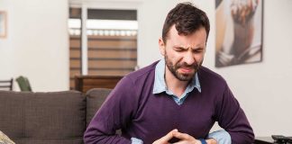 Man sitting on couch, holding stomach in pain