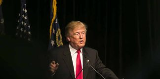 Man speaking at podium with flags in background