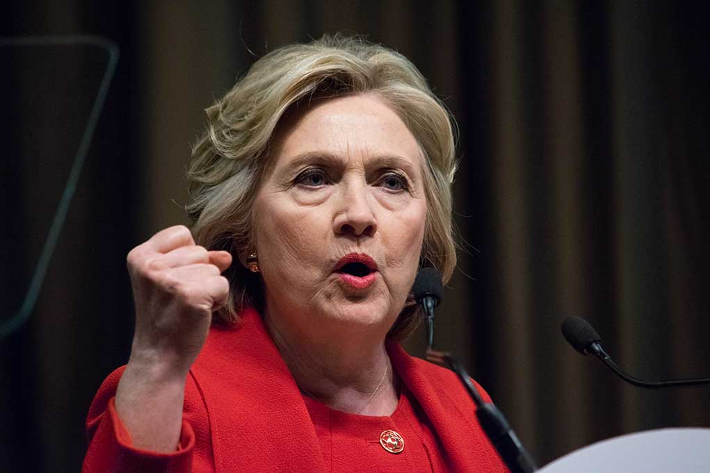 Person speaking passionately at a podium, wearing red jacket.