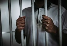 Person holding jail cell bars tightly