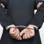 Person handcuffed in suit escorted by two others