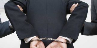 Person handcuffed in suit escorted by two others