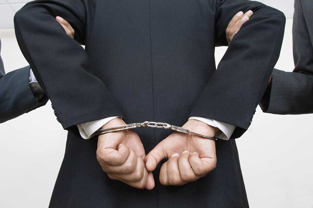 Person handcuffed in suit escorted by two others