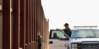 Border patrol agents near a tall metal fence