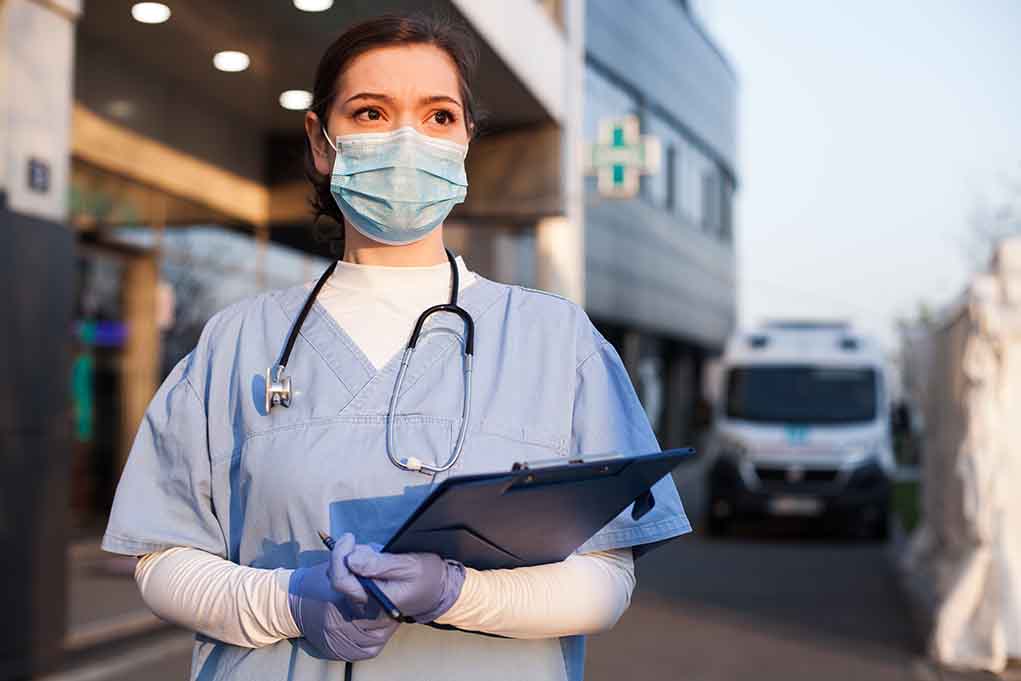 Doctor wearing mask and gloves holding clipboard outside hospital