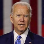 Man in suit speaking with American flag background