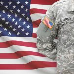 Soldier in camouflage uniform standing before American flag