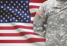 Soldier in camouflage uniform standing before American flag