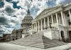 Capitol building with columns and cloudy sky.