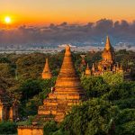 Sunset over ancient temple complex with lush greenery.