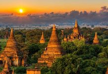 Sunset over ancient temple complex with lush greenery.
