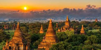 Sunset over ancient temple complex with lush greenery.