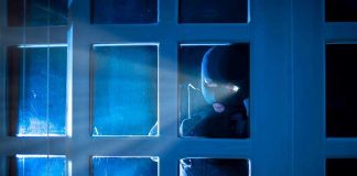 Masked figure peering through glass door at night