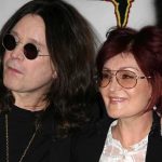 A celebrity couple posing together at an event, both wearing sunglasses and smiling