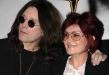 A celebrity couple posing together at an event, both wearing sunglasses and smiling