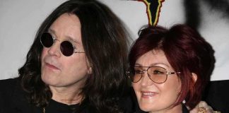 A celebrity couple posing together at an event, both wearing sunglasses and smiling