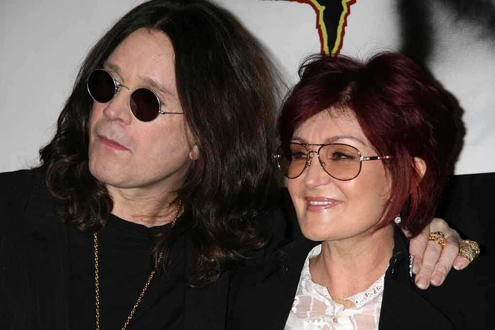 A celebrity couple posing together at an event, both wearing sunglasses and smiling