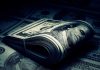 A rolled stack of hundred-dollar bills on a background of more banknotes