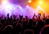 Crowd at a concert with raised hands and colorful stage lights