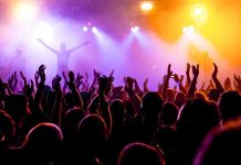 Crowd at a concert with raised hands and colorful stage lights