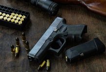 Handgun with ammunition, magazine, and rifle on wooden table.
