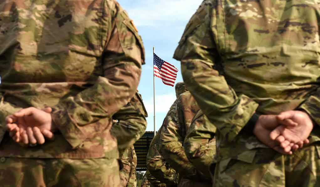 Soldiers stand in formation with American flag in background