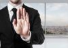 Person in suit with hand raised in stop gesture.