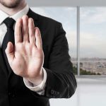 Person in suit with hand raised in stop gesture.