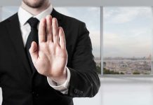 Person in suit with hand raised in stop gesture.