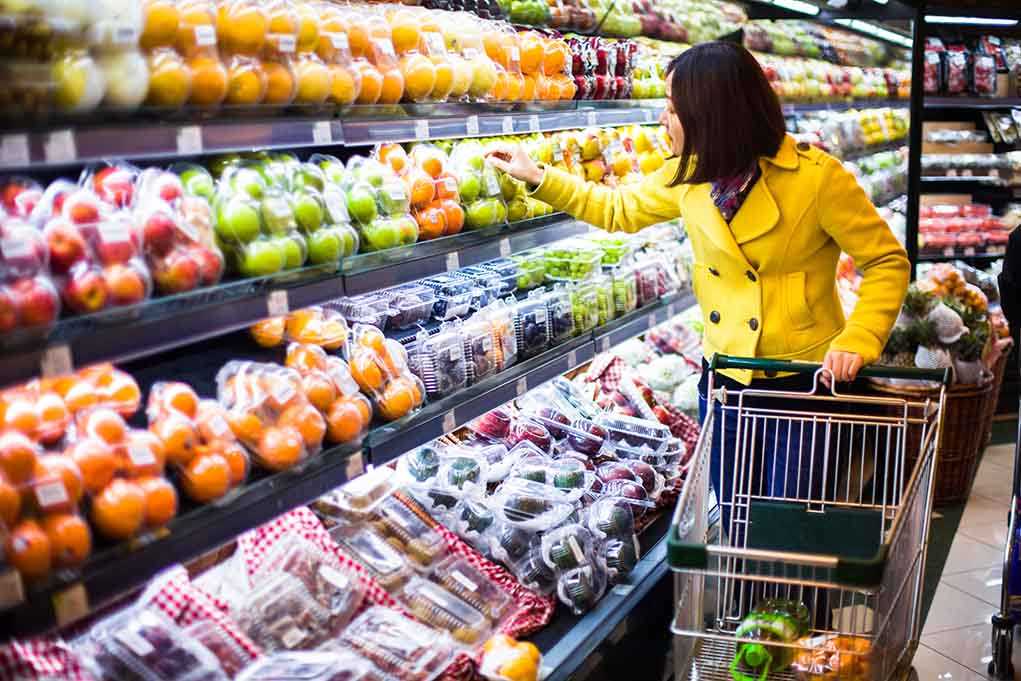 Woman in a yellow coat shopping for fruits in a supermarket