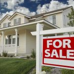A suburban house with a For Sale sign in the front yard