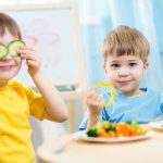 Two children playing with vegetables while enjoying a meal