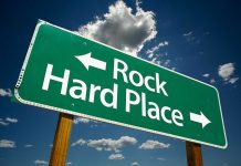 Directional road sign indicating Rock to the left and Hard Place to the right against a blue sky