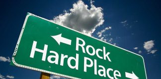 Directional road sign indicating Rock to the left and Hard Place to the right against a blue sky