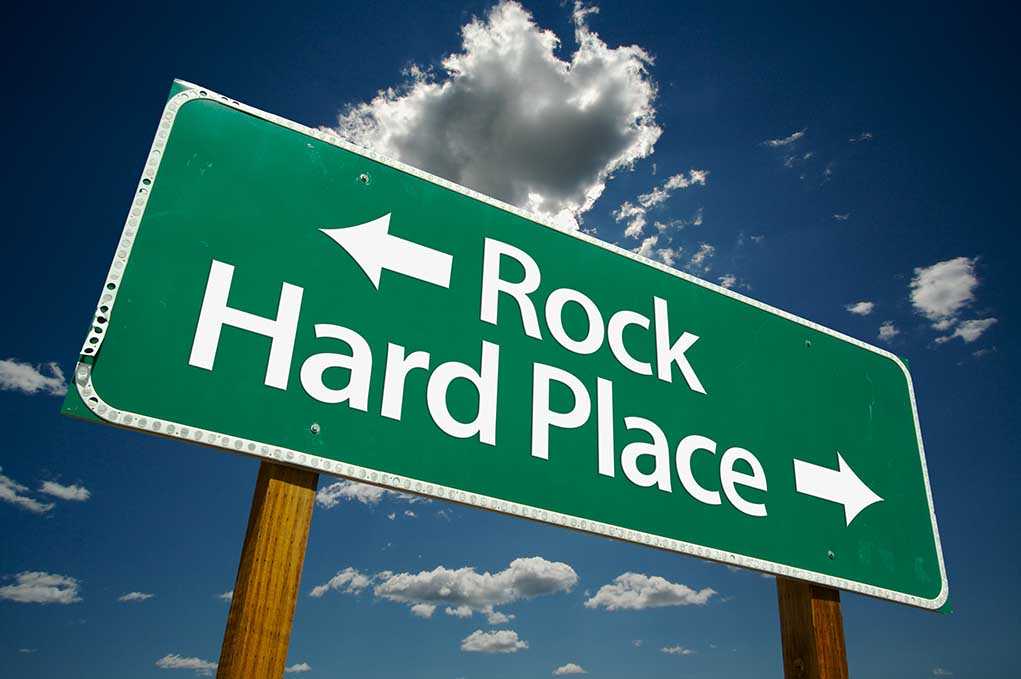Directional road sign indicating Rock to the left and Hard Place to the right against a blue sky