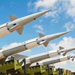 Multiple missiles pointed upward on launchers against blue sky