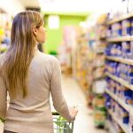 A woman pushing a shopping cart in a supermarket aisle filled with products