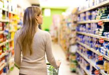 A woman pushing a shopping cart in a supermarket aisle filled with products