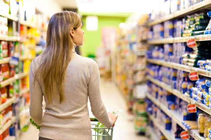 shutterstock_121990036.jpg A woman pushing a shopping cart in a supermarket aisle filled with products