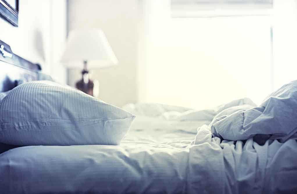 A cozy unmade bed with soft pillows and bedding in a well lit room