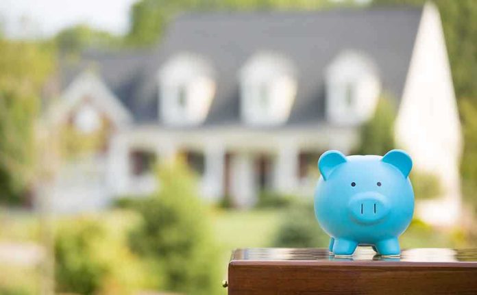 shutterstock_219244759.jpg A blue piggy bank in front of a blurred house and greenery