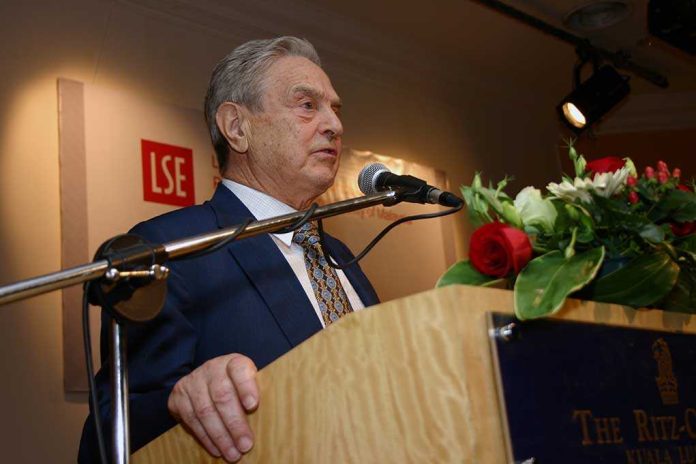 A man in a suit speaking at a podium with flowers and a microphone