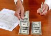 Hands counting cash and reviewing financial documents on a wooden table
