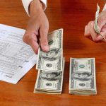 Hands counting cash and reviewing financial documents on a wooden table