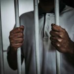 Person holding jail cell bars tightly