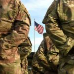 Soldiers stand in formation with American flag in background